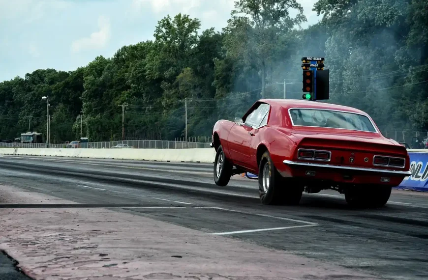 Drag racing car in pit lane with a technician inspecting the exhaust setup