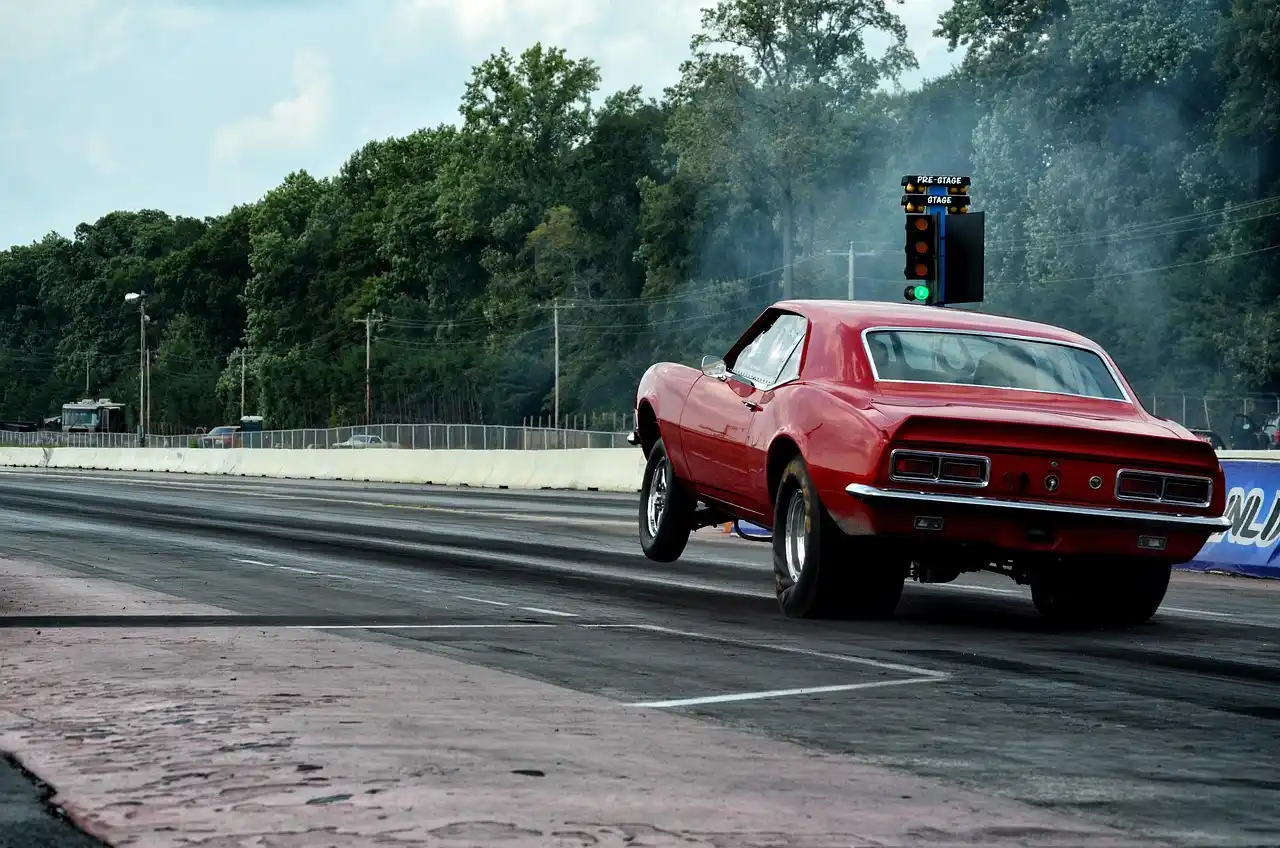 Drag racing car in pit lane with a technician inspecting the exhaust setup