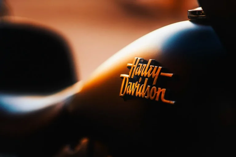 Motorcyclist inspecting a loud aftermarket motorcycle exhaust beside a parked bike at golden hour.