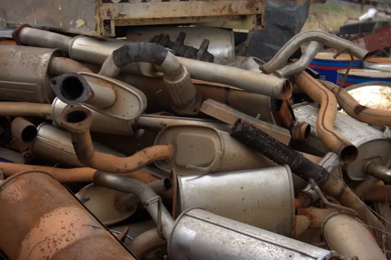 Mechanic inspecting a rusted exhaust pipe and muffler under a lifted car in a bright garage
