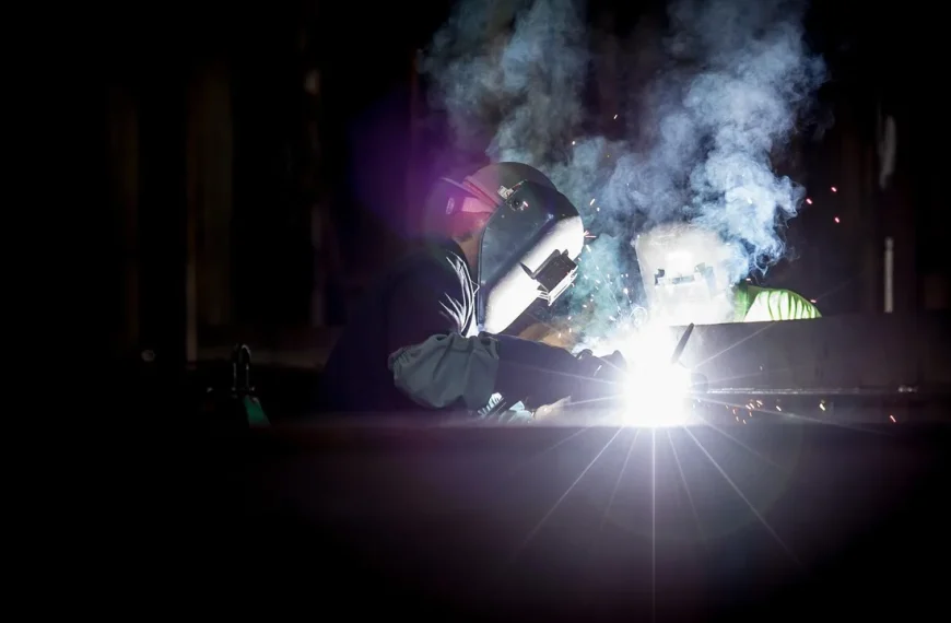 Mechanic comparing a welder beside exhaust pipe sections and stainless tubing in a garage