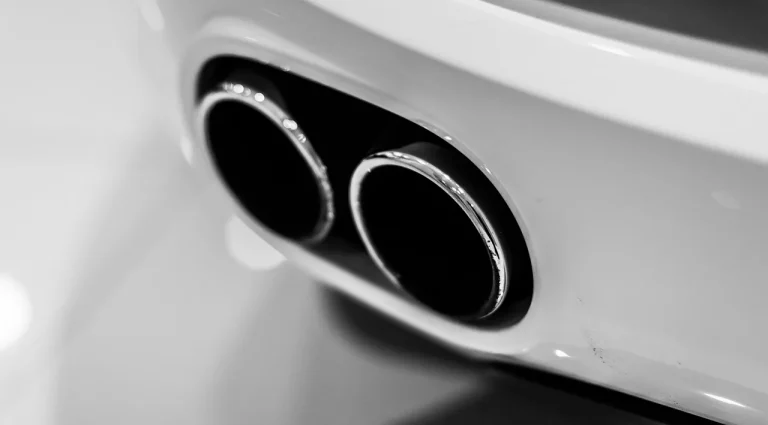Car rear with black coated and polished exhaust tips being wiped clean in daylight