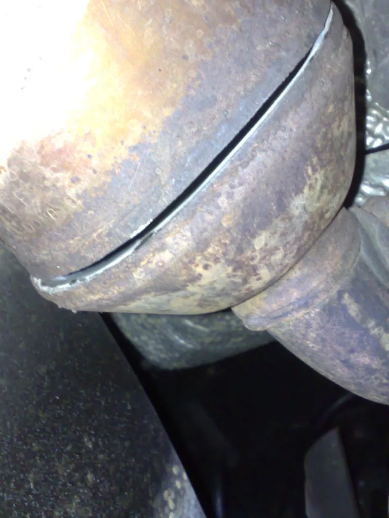 Mechanic comparing catalytic converter parts next to a compact car, SUV, and performance sedan in a repair shop
