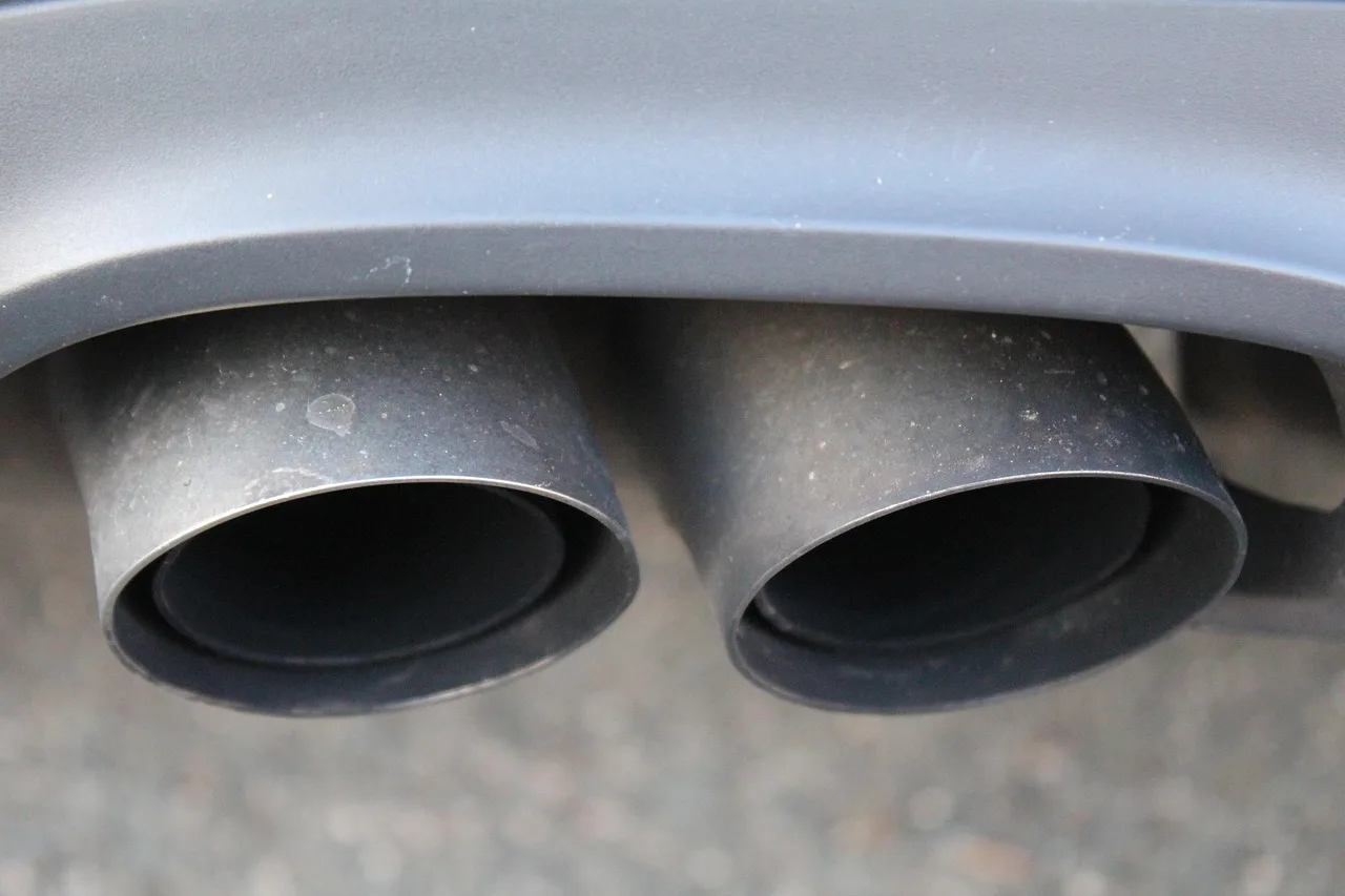 Turbocharged sedan on a lift with a mechanic comparing catted and catless downpipes.