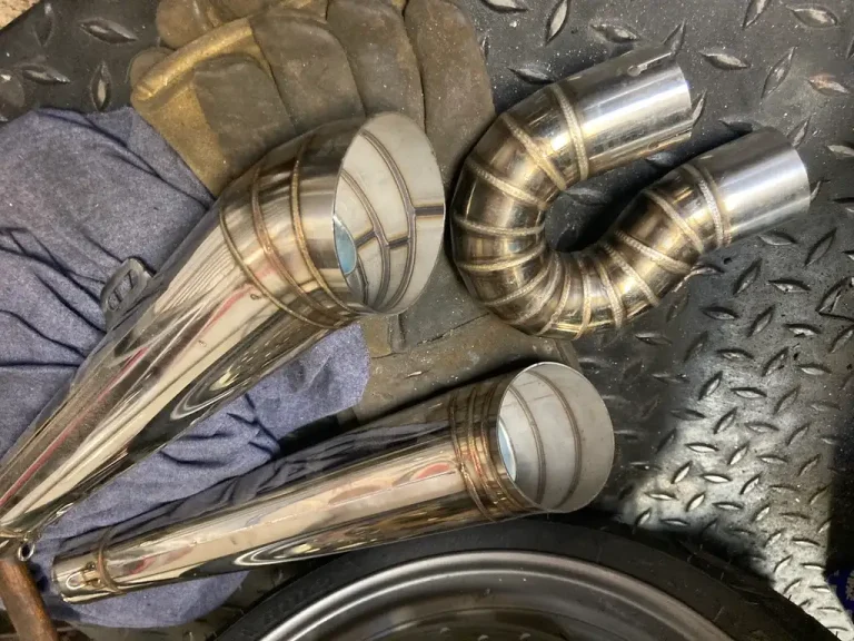 Mechanic comparing an exhaust manifold and a tubular header beside a pickup in a shop