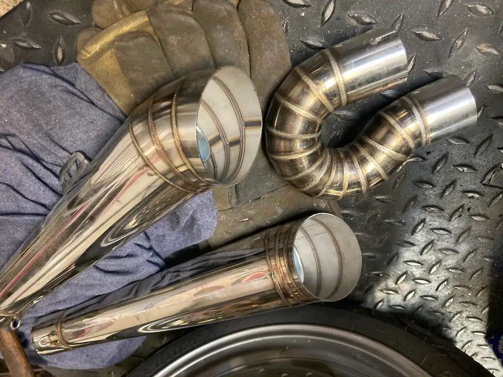 Mechanic comparing an exhaust manifold and a tubular header beside a pickup in a shop