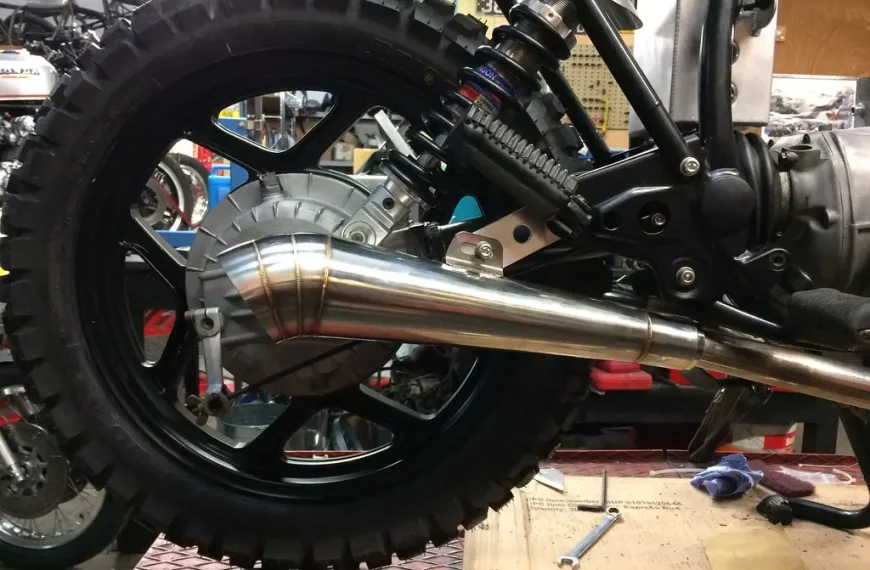 Mechanic comparing two exhaust pipe ends on a workbench, with clamps and a tape measure.