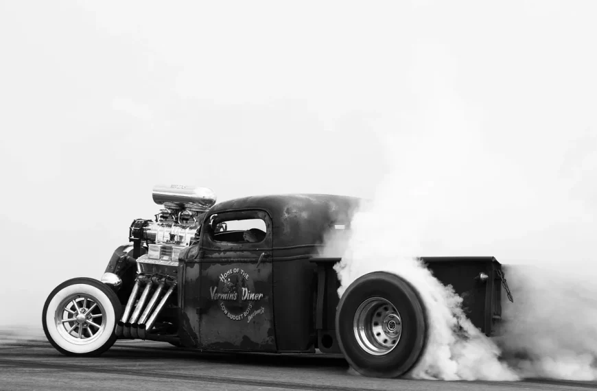 Mechanic observing light blue exhaust smoke near a car tailpipe in a garage