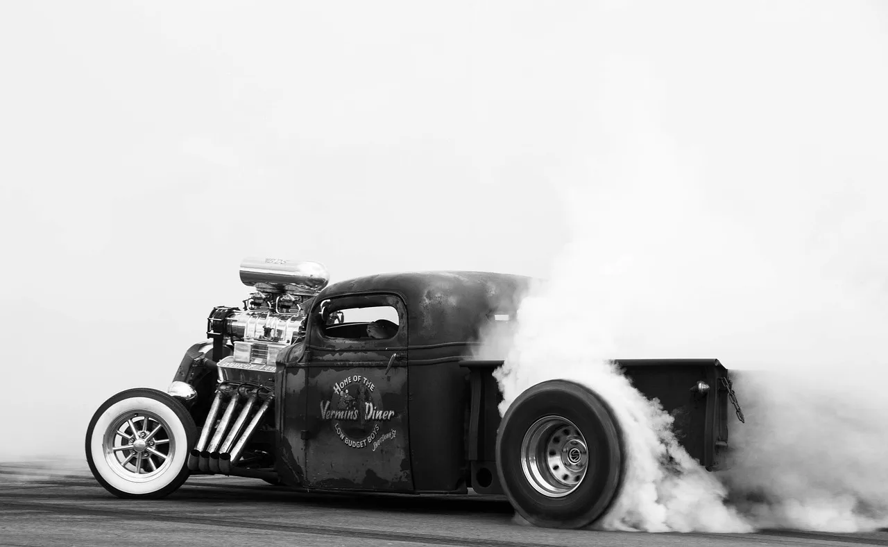 Mechanic observing light blue exhaust smoke near a car tailpipe in a garage