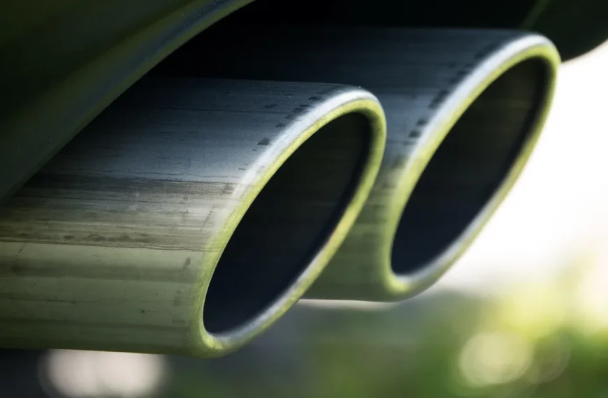 Mechanic and car owner inspect an exhaust system under a lifted car in a sunlit garage