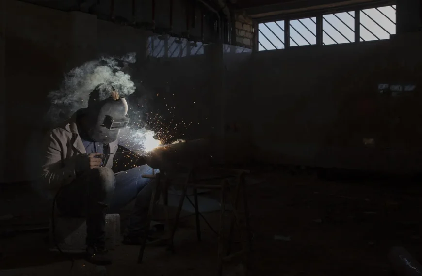 Mechanic under a lifted car measuring exhaust tubing in a bright auto shop