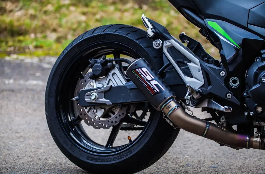 Motorcycle rider comparing exhaust parts on a garage workbench beside the bike
