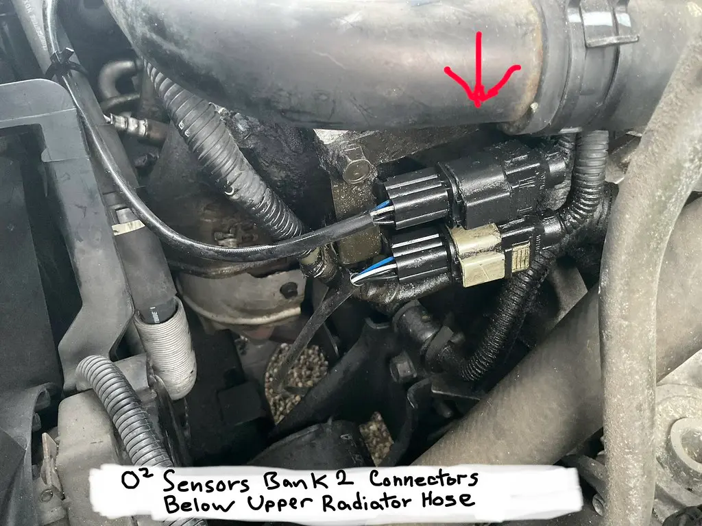 Mechanic comparing OEM and aftermarket oxygen sensors beside a car in a repair shop