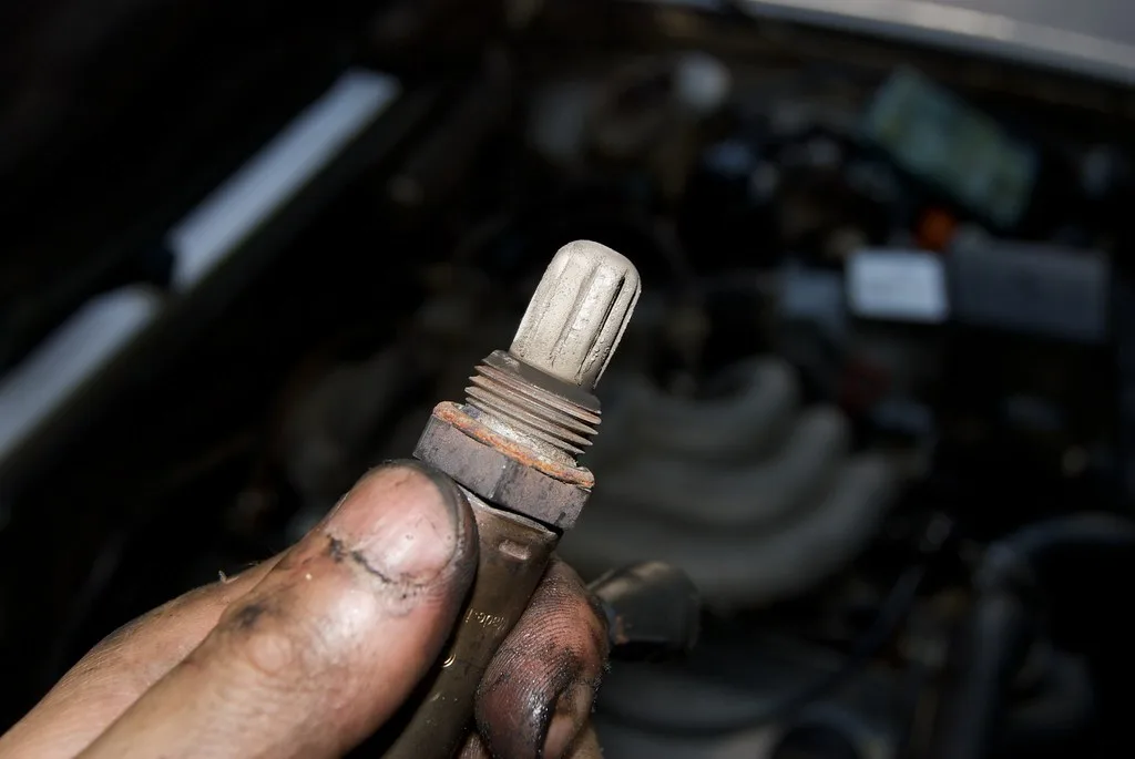 Multimeter probes testing an oxygen sensor connector beside an exhaust pipe