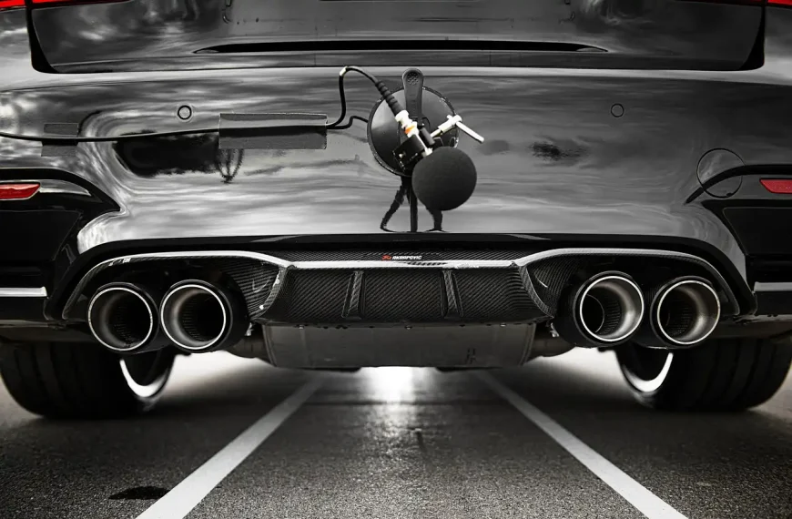 Mechanic and car owner inspecting a sedan's exhaust under the rear bumper in a garage