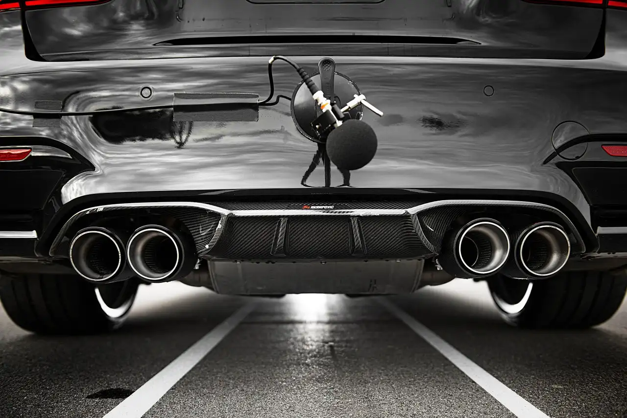 Mechanic and car owner inspecting a sedan's exhaust under the rear bumper in a garage