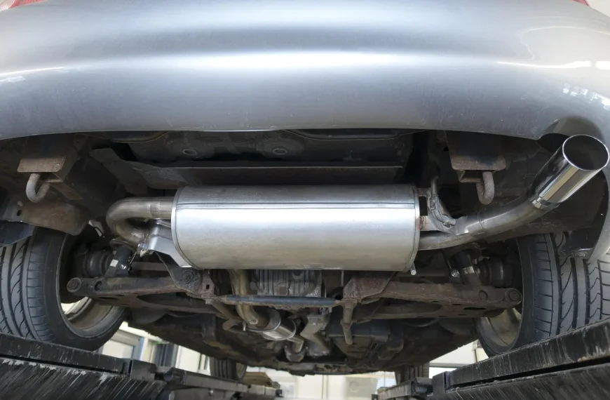 Mechanic inspects a car exhaust system on a lift, showing pipes, catalytic converter, muffler, and tailpipe.