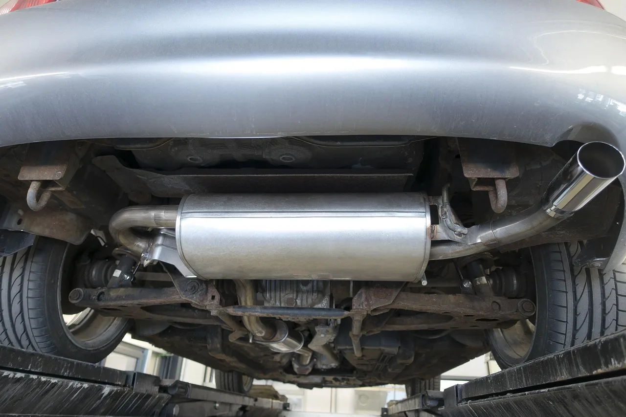 Mechanic inspects a car exhaust system on a lift, showing pipes, catalytic converter, muffler, and tailpipe.