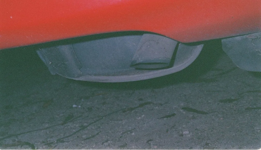 Close-up of a corroded exhaust pipe joint and clamp being checked under a car.